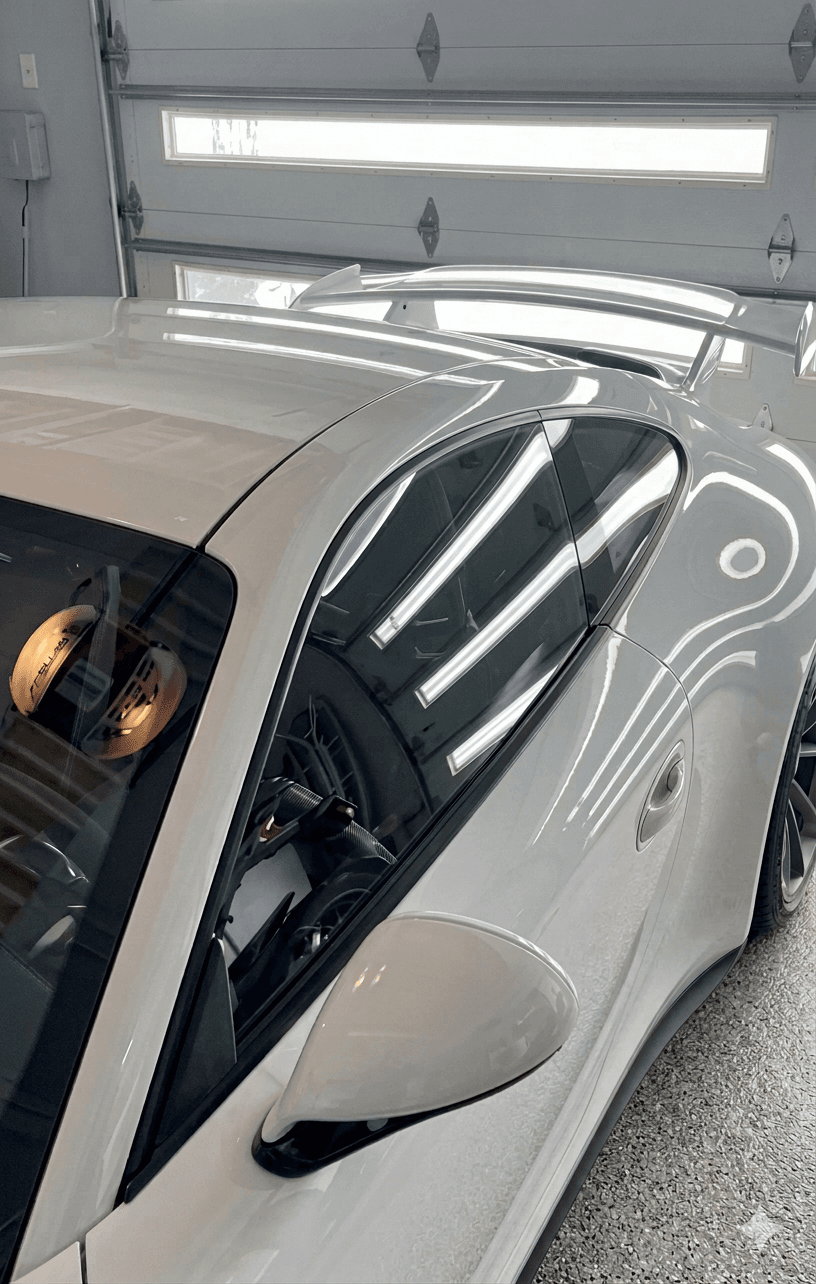 High-angle view of a glossy white Porsche sports car with a rear wing parked on an epoxy garage floor