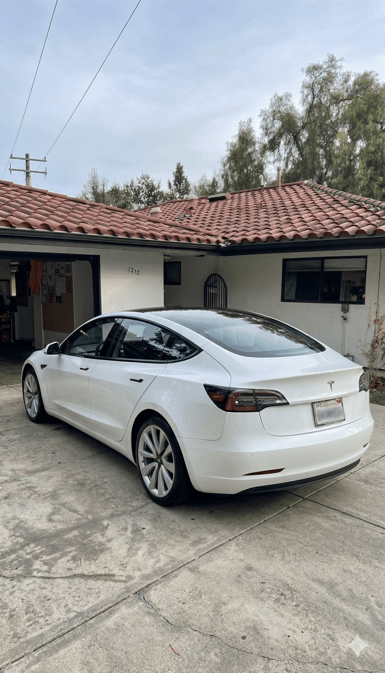 Pearl white Tesla Model 3 parked on a concrete driveway in front of a terracotta-roof home