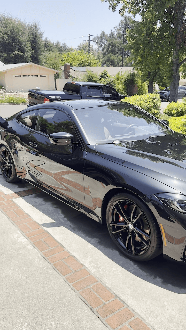 Glossy black BMW coupe on a brick-edged concrete driveway with red brake calipers visible through black alloy wheels