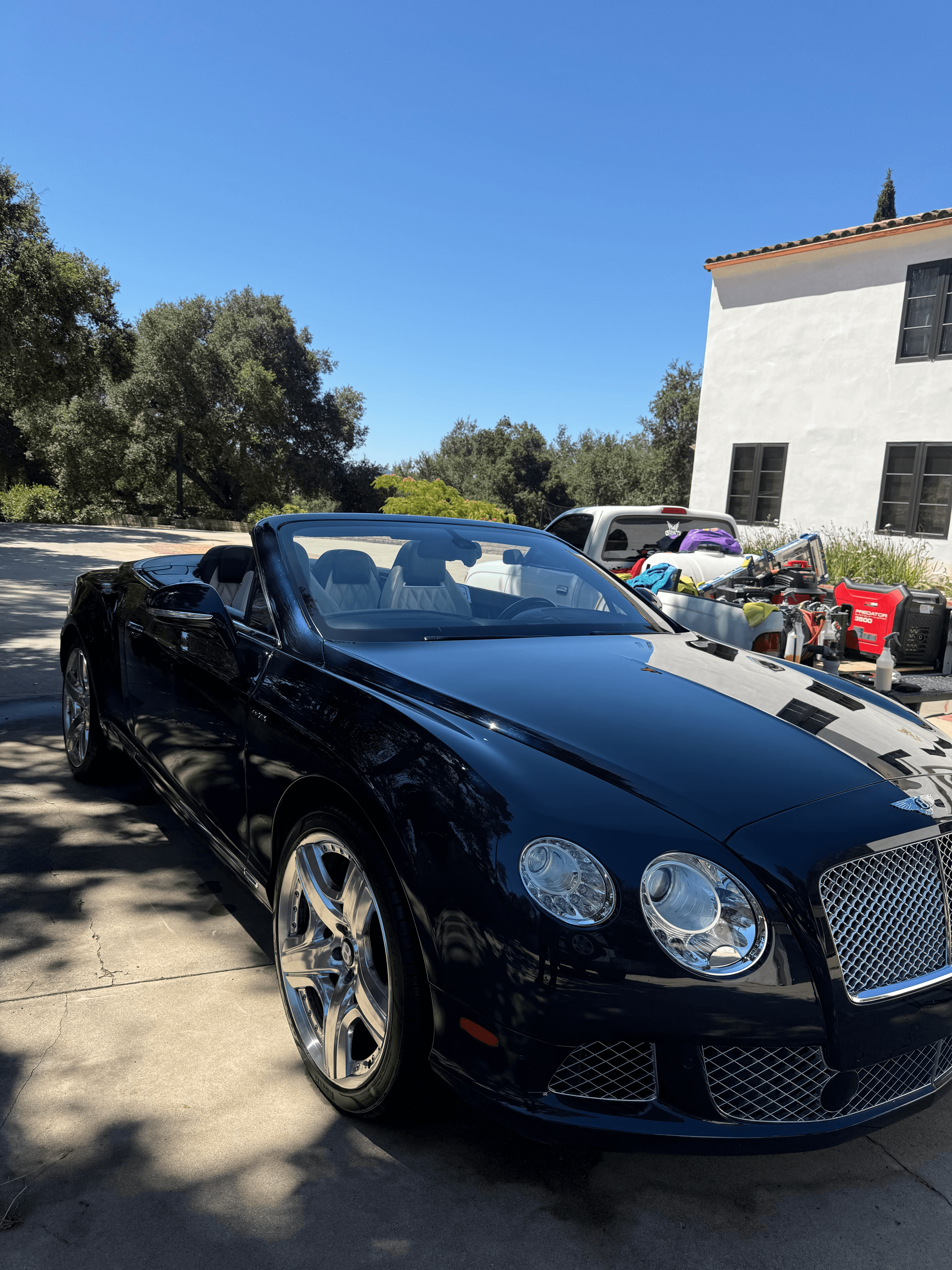 Dark blue Bentley Continental GTC convertible with the top down, showing mirror-like paint reflections on a sunny driveway