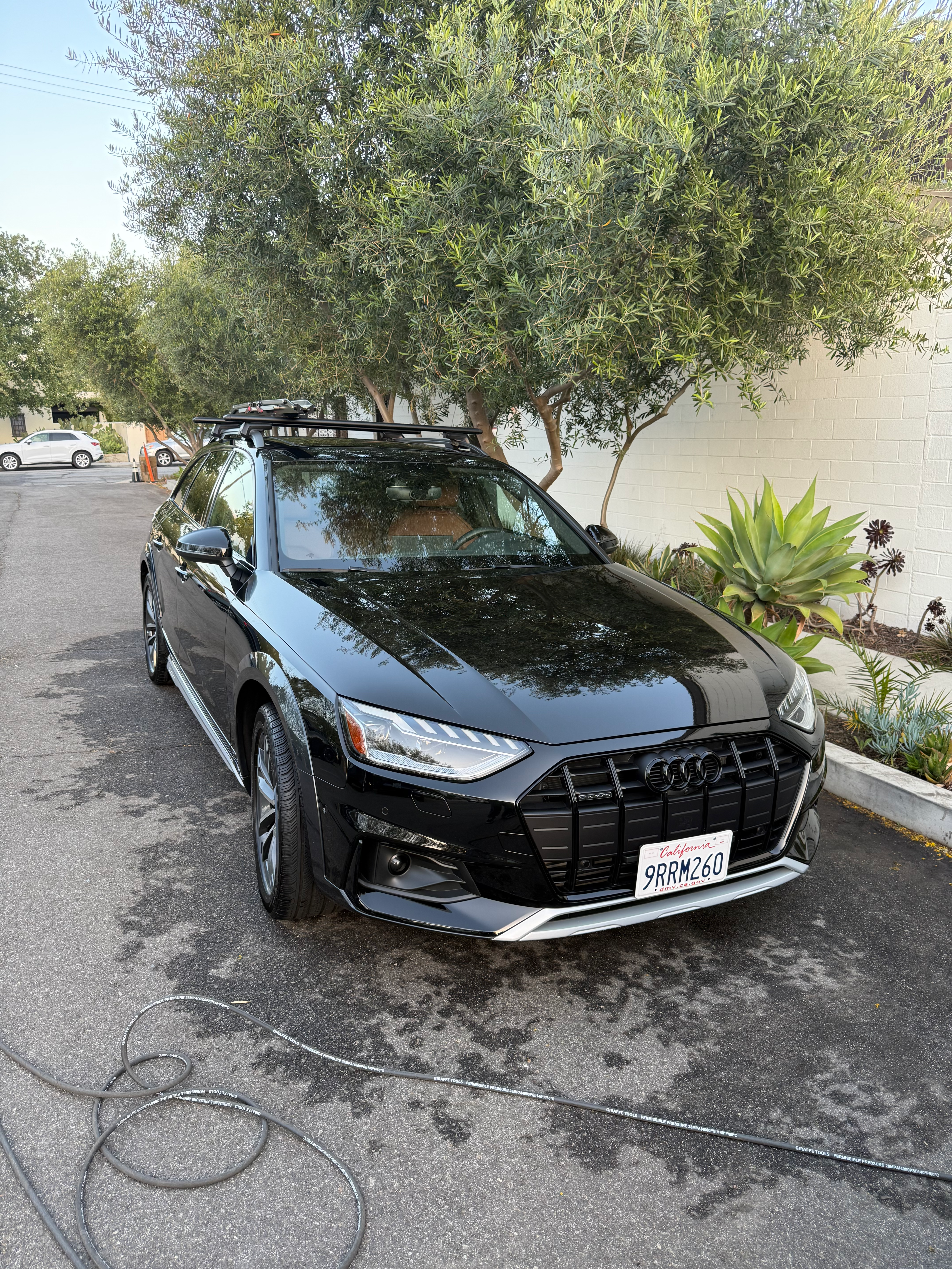 Glossy black Audi A4 Allroad wagon on an asphalt driveway with roof rails and a freshly washed exterior