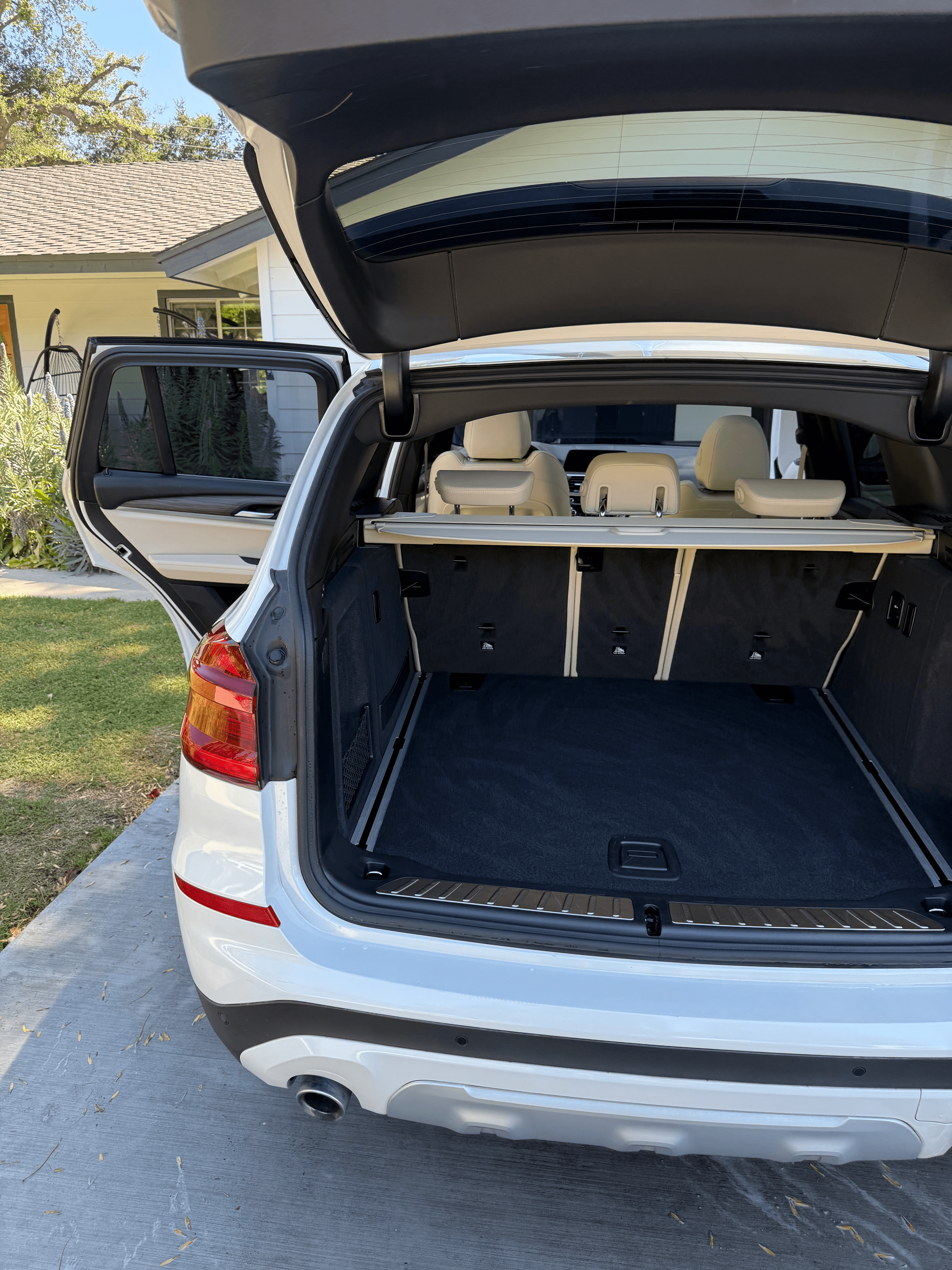 White BMW SUV with the rear hatch and door open, showing a vacuumed and cleaned cargo area on a residential driveway