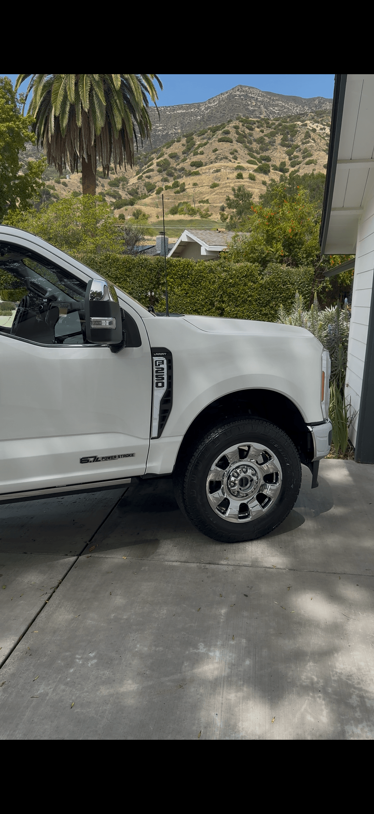 White Ford F-250 Lariat pickup on a concrete driveway in bright sunlight with a clean, glossy cab and chrome wheels