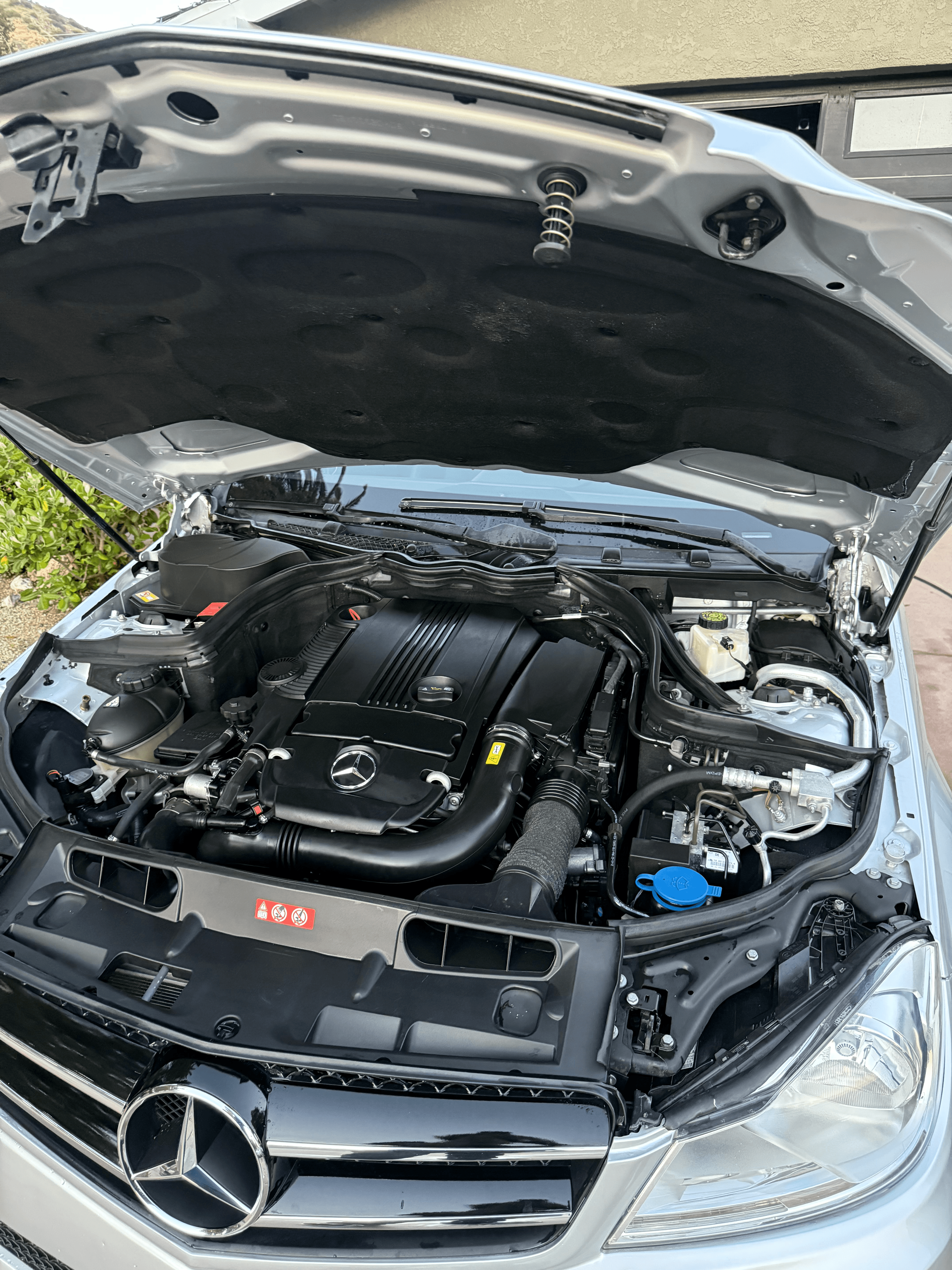 Silver Mercedes-Benz with the hood open, showing a cleaned and dressed engine bay on a paved driveway