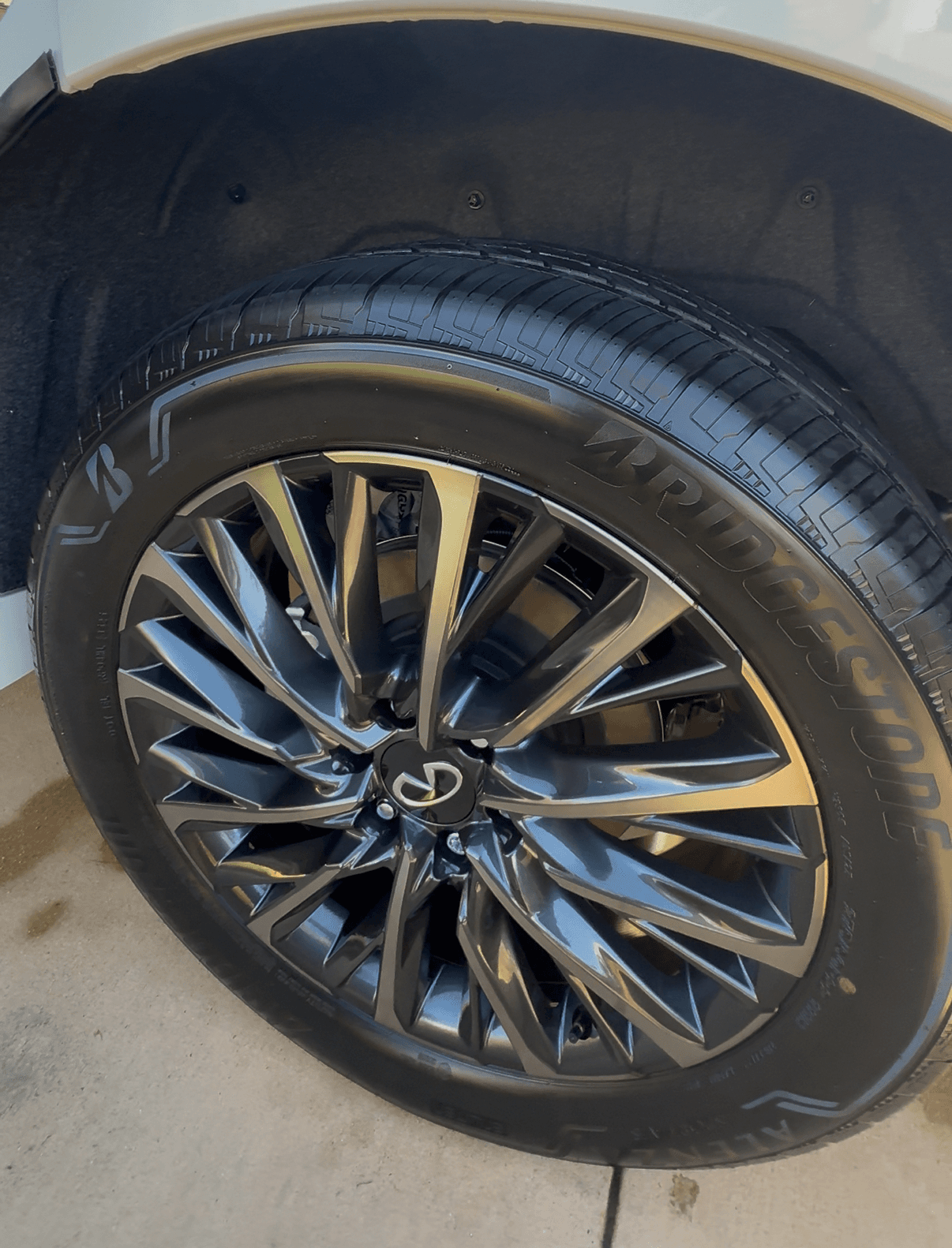 Close-up of a dark multi-spoke Infiniti alloy wheel and Bridgestone tire with a glossy, freshly detailed finish